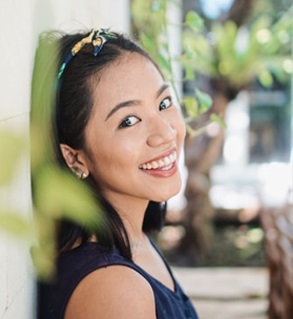 A photo of a smiling Asian woman leaning against a wall