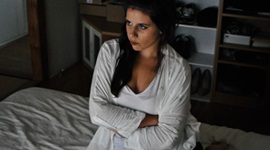 A photo of a woman sitting in bed with her arms crossed